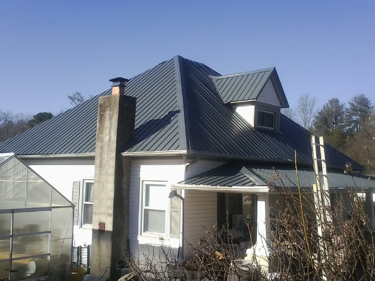 Dark blue standing seam metal roof on a white farmhouse with dormer — Slate & Tile Roof Repair by Roofing Brothers in Cliffside Park