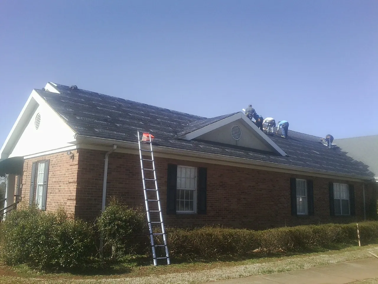 Crew tearing shingles off a brick ranch roof with a ladder set — Emergency Roof Repair work by our crew in Cliffside Park