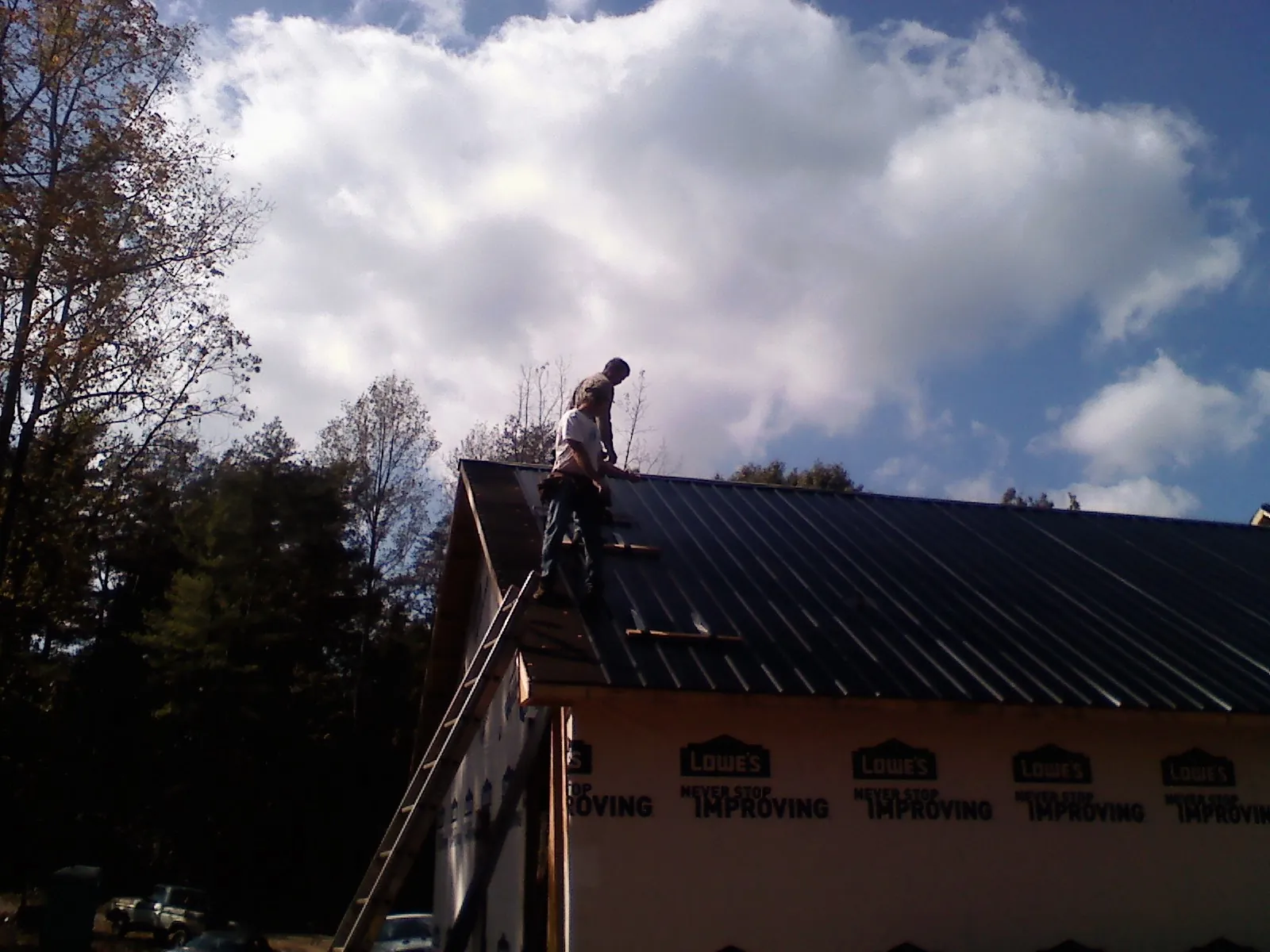 Roofer fastening dark metal panels high against a cloudy sky, from a Roof Inspection job in Cliffside Park