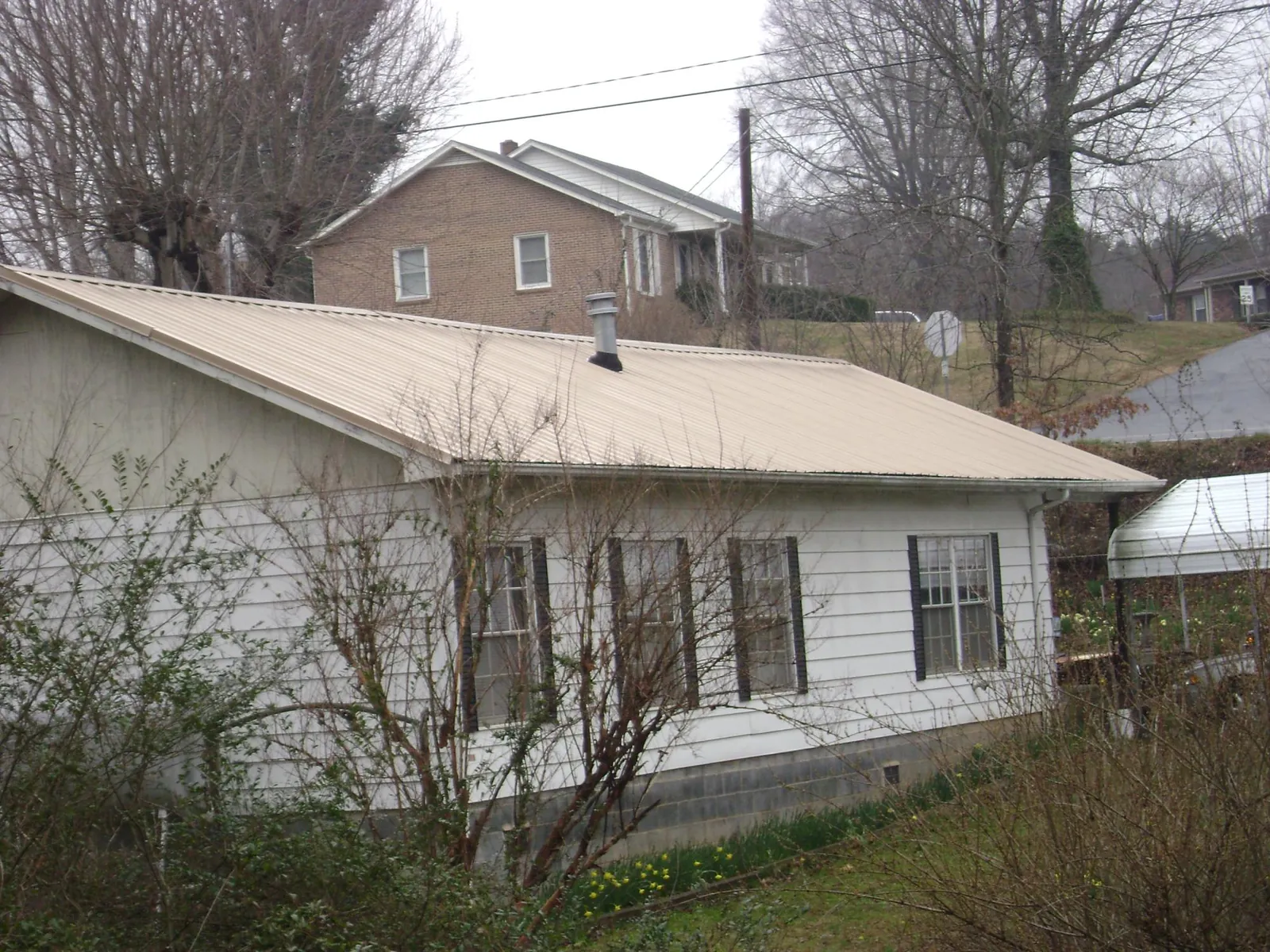 Tan metal roof on a white sided house set into a hillside — Commercial Roofing by Roofing Brothers in Cliffside Park